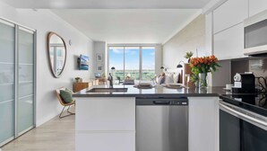 A modern kitchen with a central island, a dishwasher, and a coffee machine. There is a large window providing a view of the outdoors. - Spectacular Bay View Apartment in Coconut Grove (Miami)