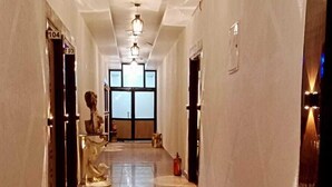 A long, well-lit hallway with a polished marble floor, doors on both sides, and a statue in the center. - Deepak Hotel (Meerut)