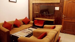 A living room with a sofa set, a coffee table, a television, and a wooden door. - Deepak Hotel (Meerut)