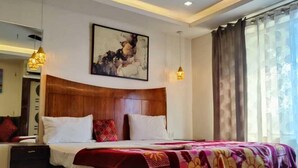 A hotel room with a bed, a ceiling fan, a painting, and a window with curtains. - Deepak Hotel (Meerut)