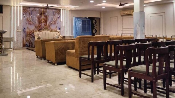A spacious hall with a high ceiling, recessed lighting, and a marble floor. There are rows of wooden chairs and sofas arranged for seating. - Deepak Hotel (Meerut)
