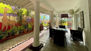 A covered outdoor area with a mural, potted plants, a dining table with chairs, and a tiled floor. - Villa Poisson Dans l 'eau (Trou aux Biches)