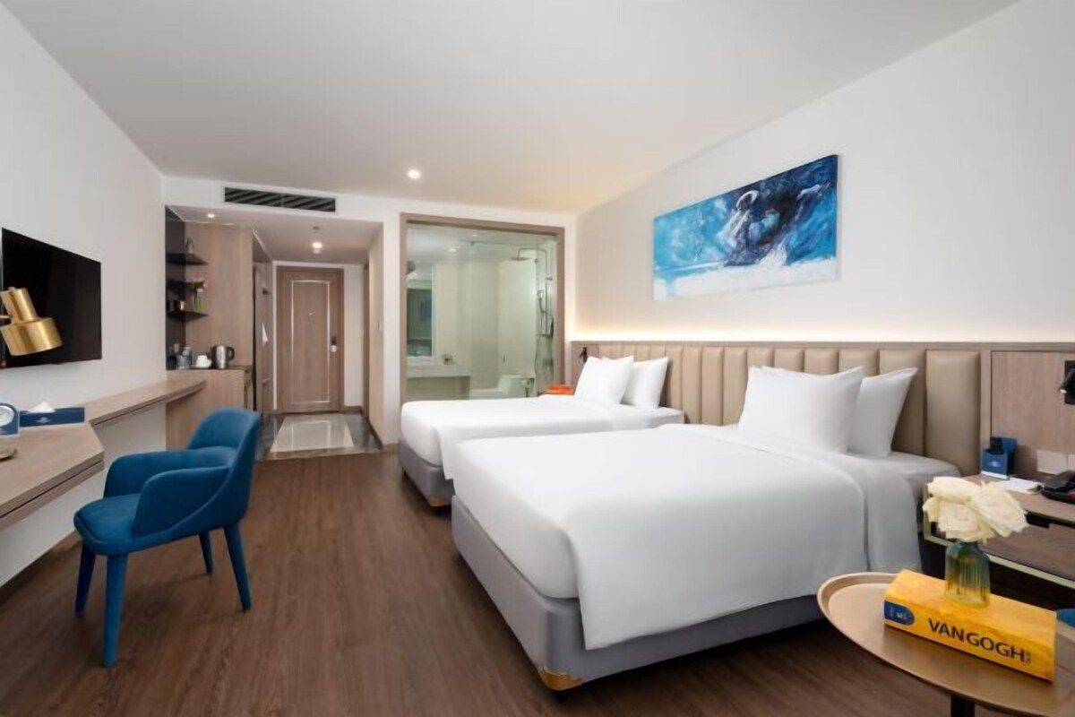 Ein Hotelzimmer mit zwei Betten, einem Schreibtisch, einem Stuhl, einem Fernseher und einem Bild an der Wand.