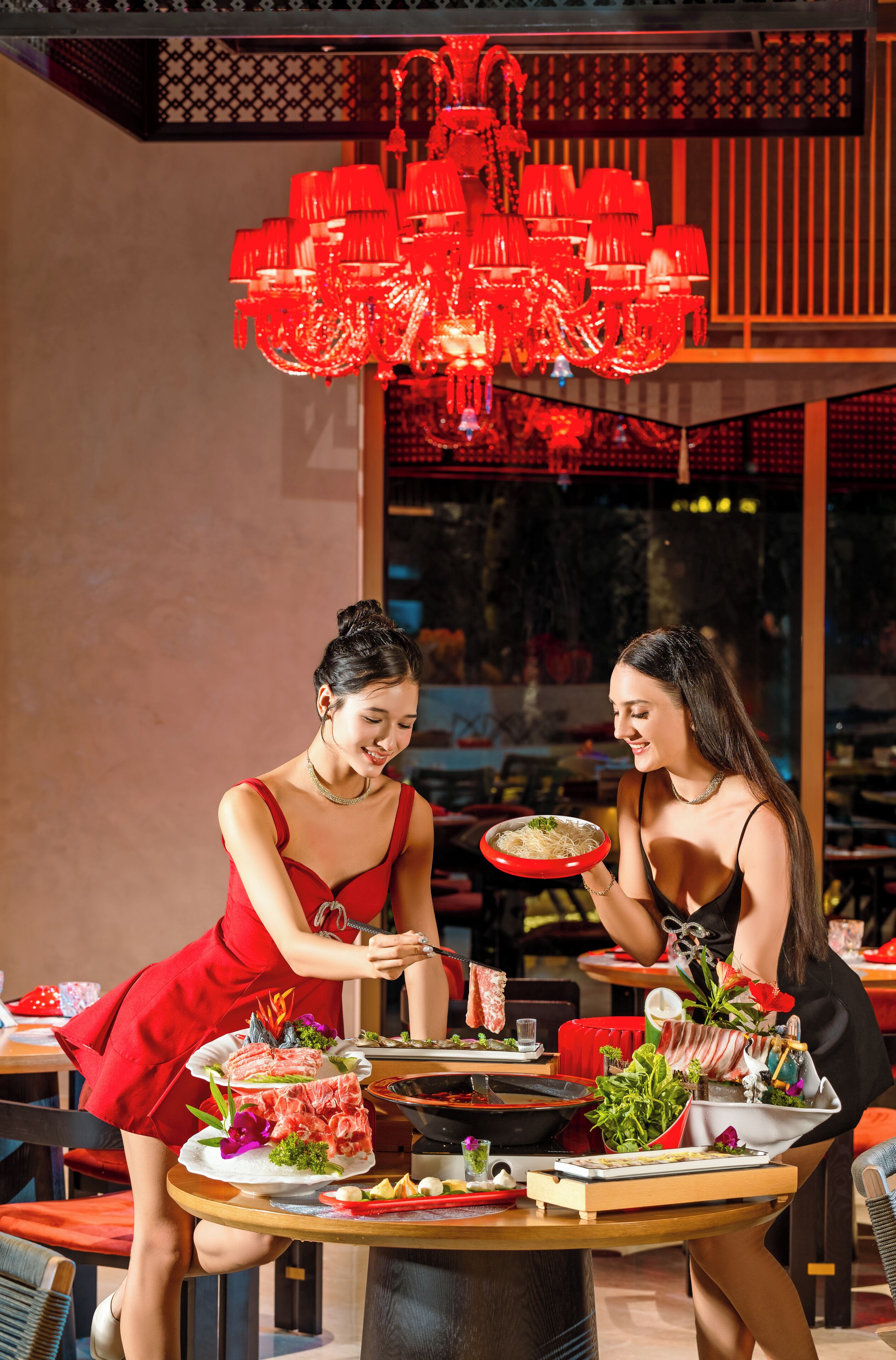 A dining area with a round table, red chairs, and a red chandelier.