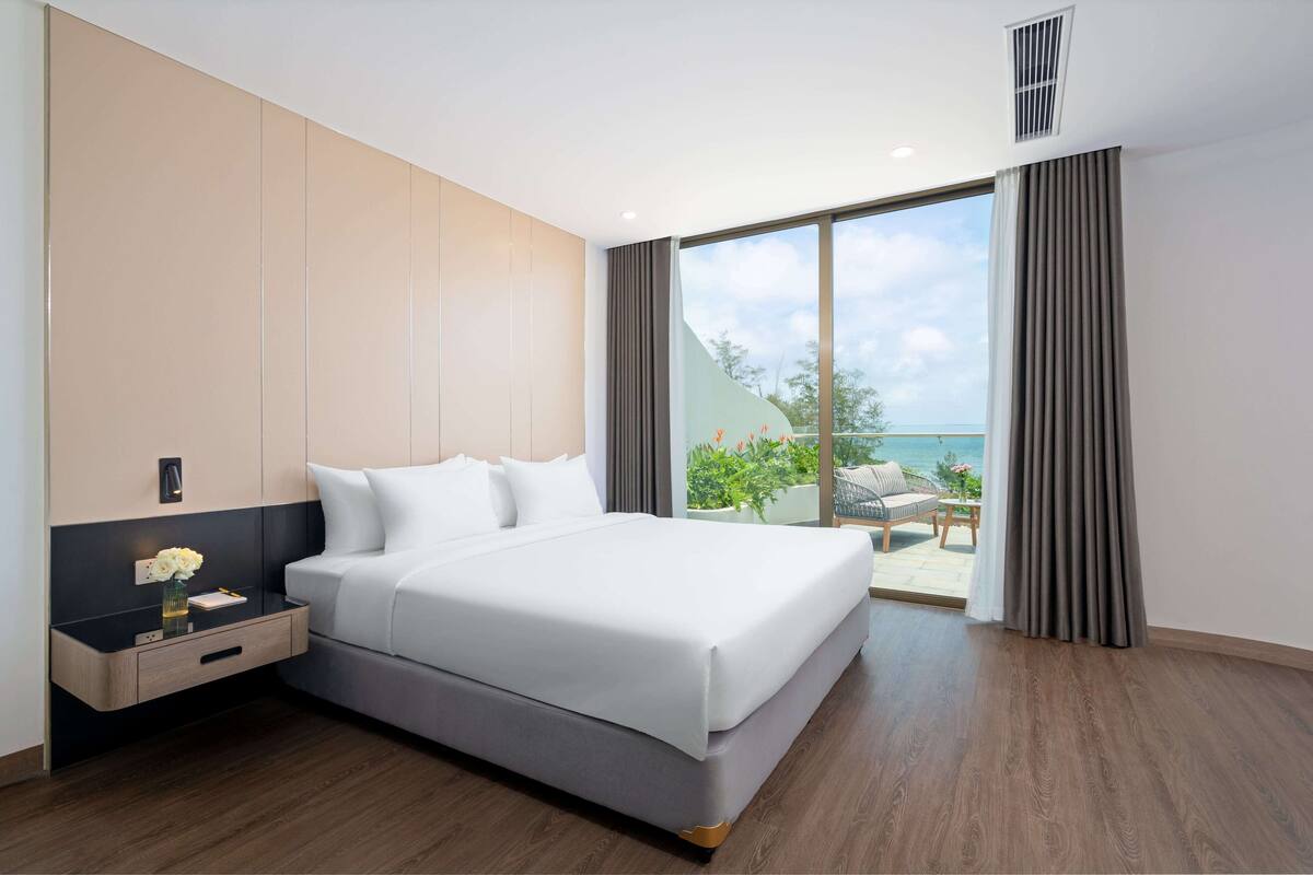 Una habitación de hotel moderna con una cama grande, una mesita de noche y vistas al exterior.