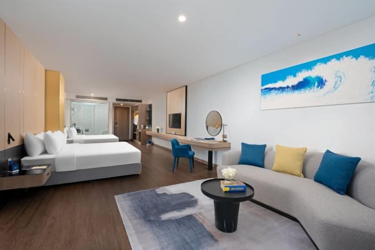 Ett modernt hotellrum med en säng, en soffa, ett skrivbord och en stor tavla som föreställer en våg.