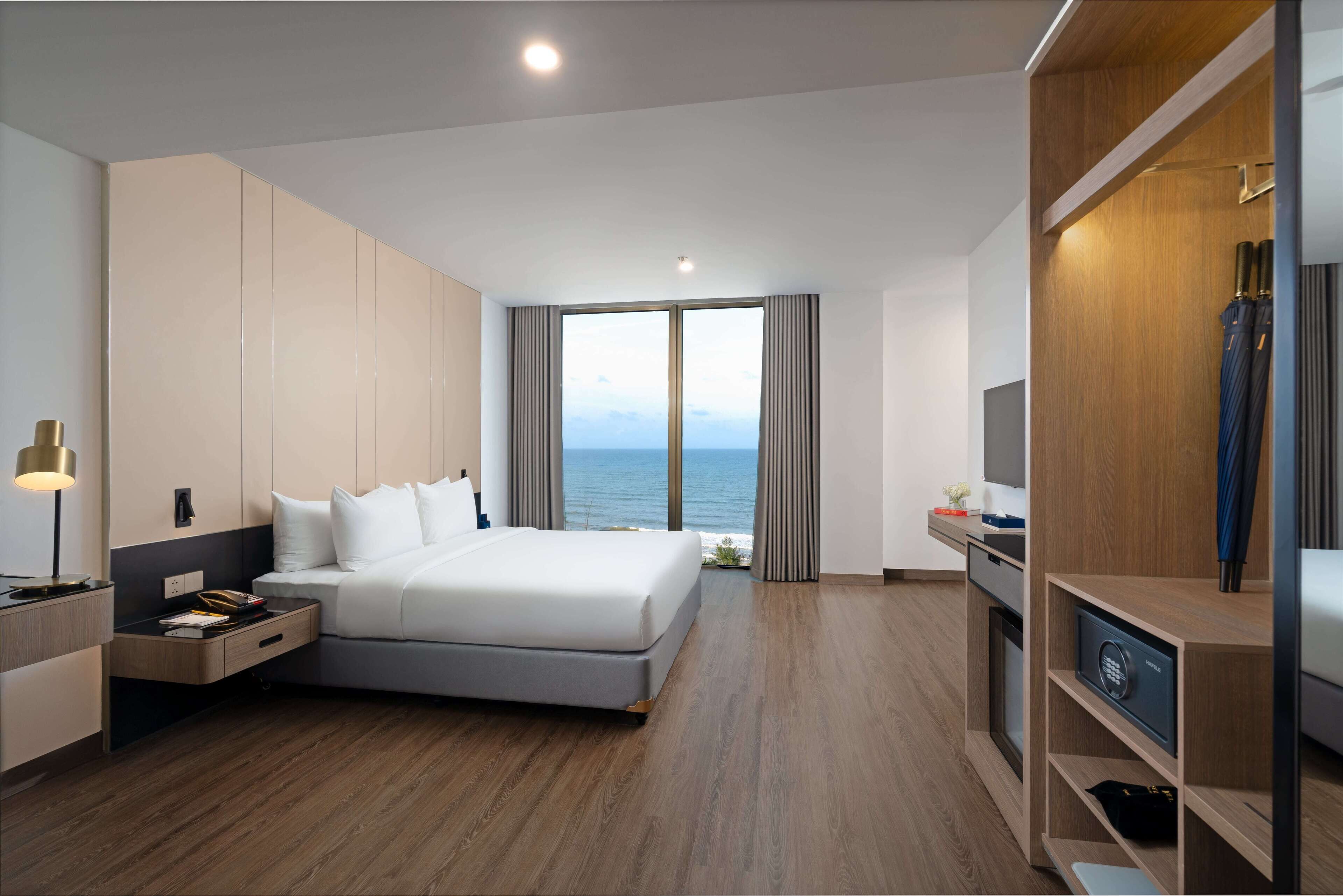 Ein modernes Hotelzimmer mit einem großen Bett, einem Schreibtisch, einem Kleiderschrank und Blick auf das Meer.