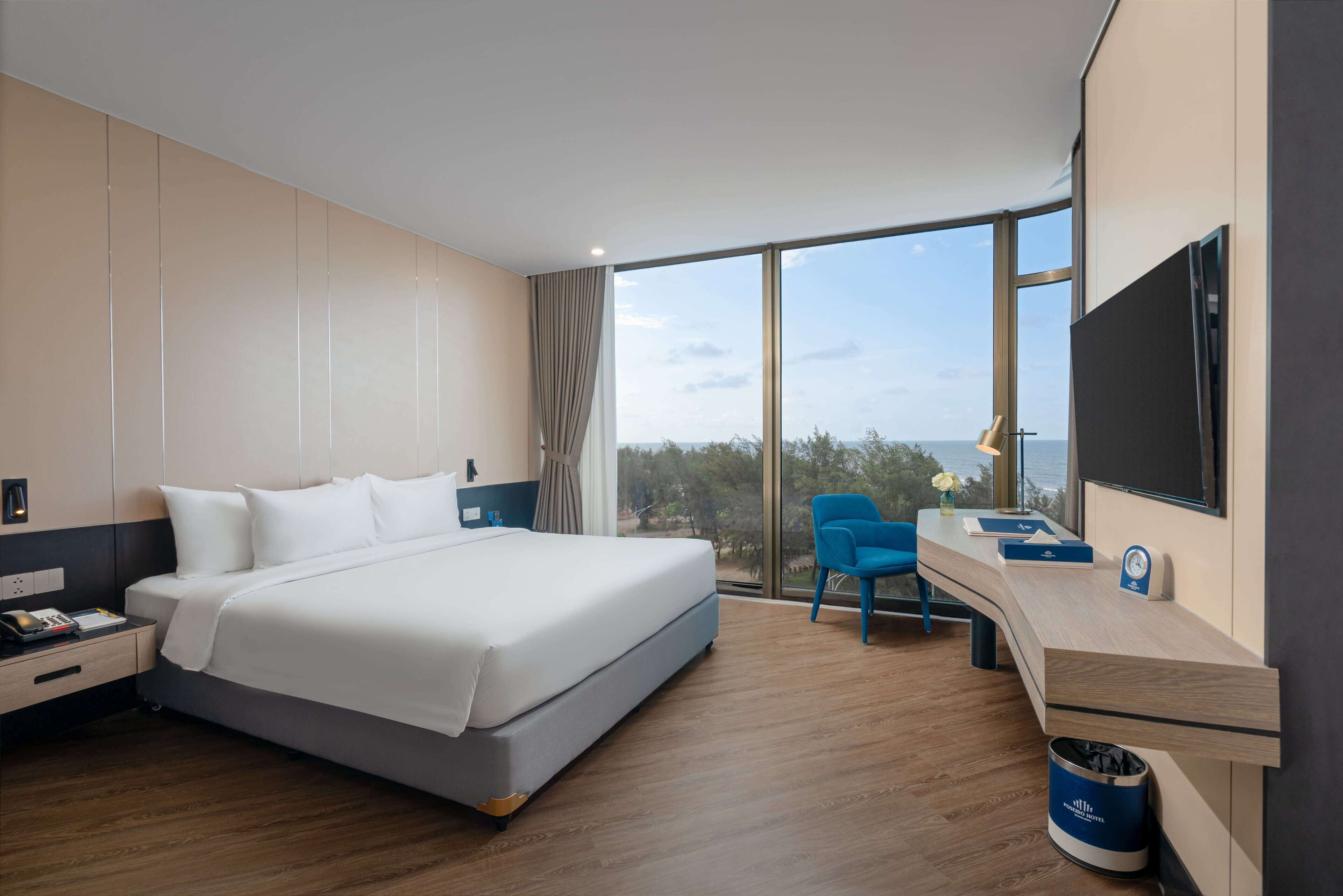 A modern hotel room with a large bed, a desk with a chair, a TV, and a view of the outdoors.