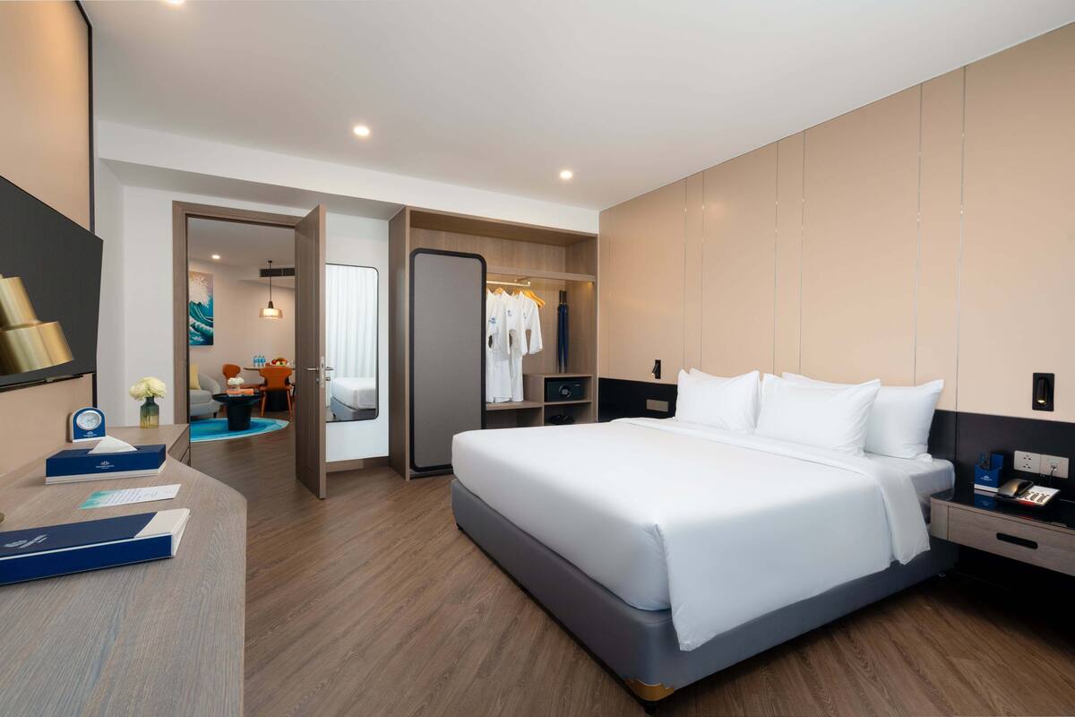 Un cuarto de hotel moderno con una cama grande, un escritorio con computadora, un armario y un baño visible a través de una puerta abierta.
