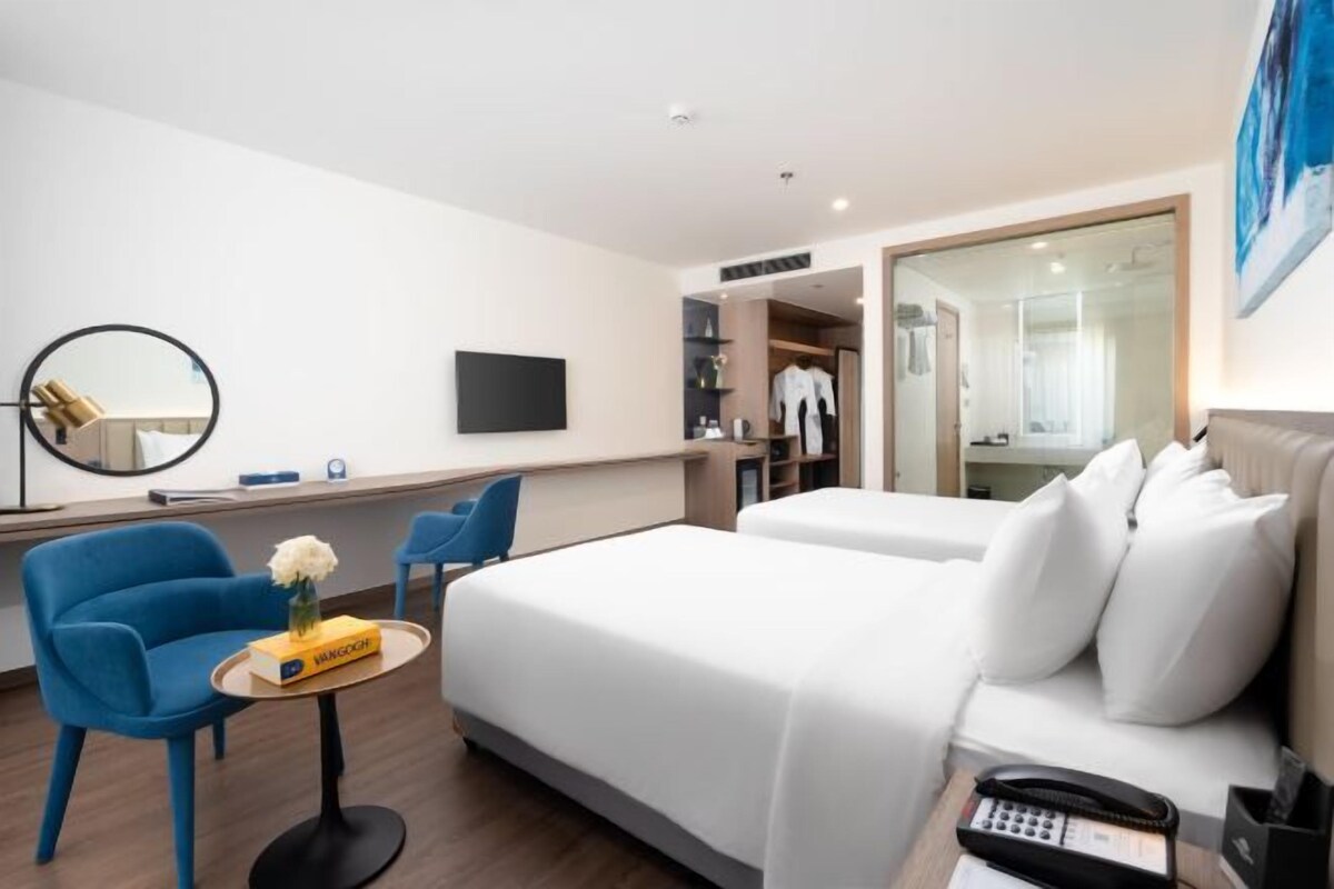 Habitación de hotel con dos camas, un escritorio, una silla, un televisor y un armario.