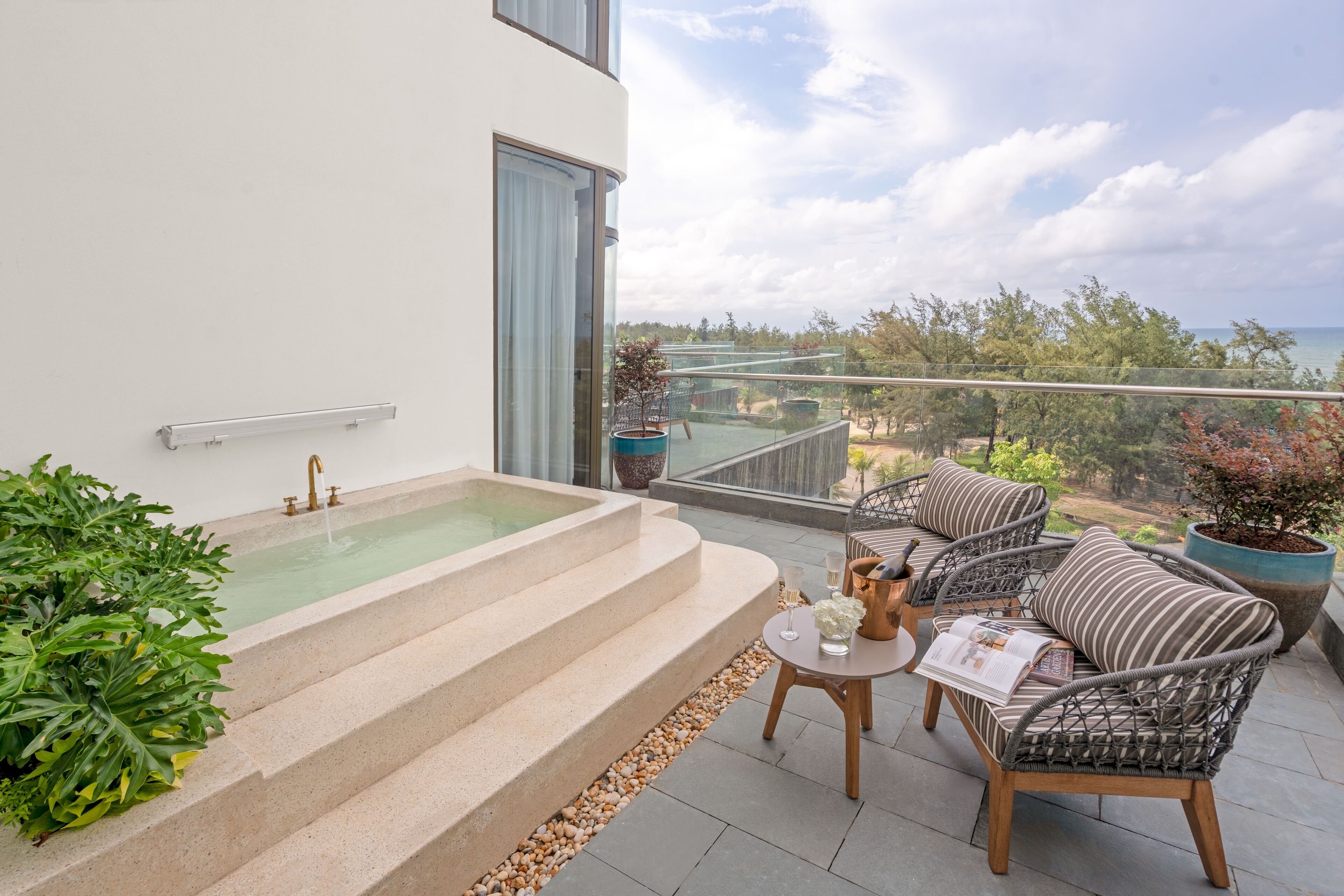 A modern outdoor balcony with a hot tub, wicker furniture, and a view of the sea.