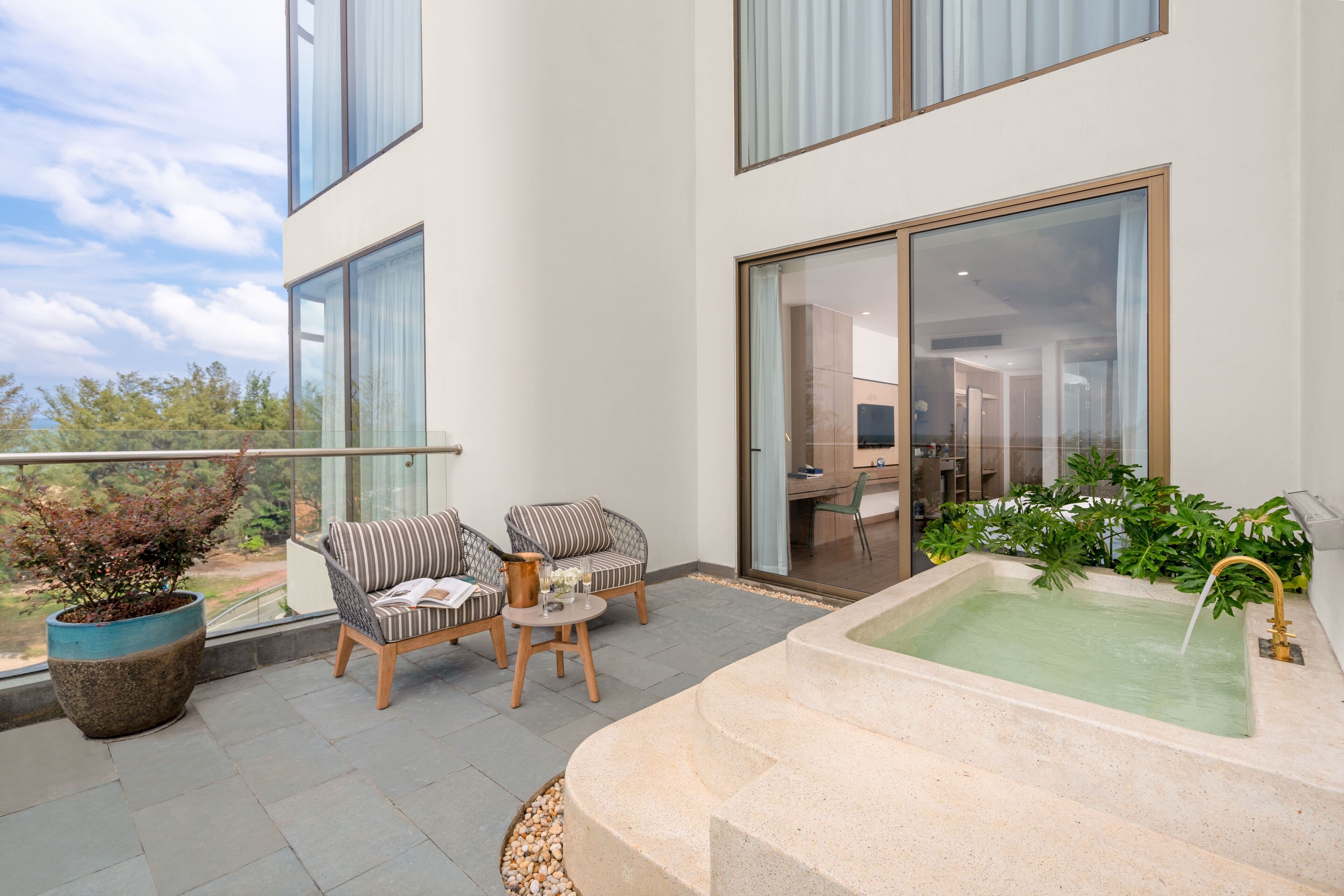 Een modern balkon met twee comfortabele stoelen, een klein tafeltje, een grote potplant en een rustgevend waterpartij.