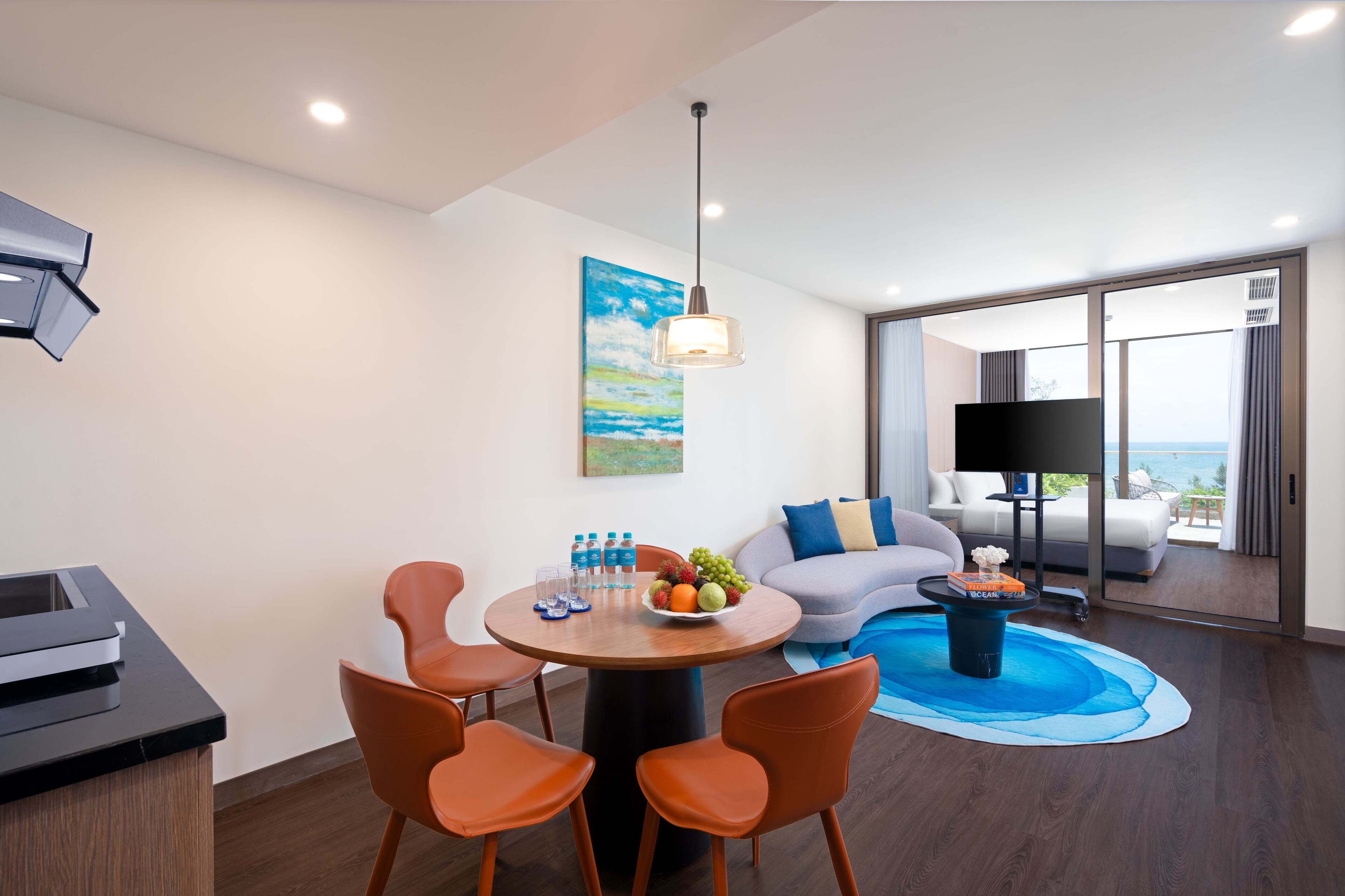 A modern hotel room with a dining area, a sofa with a view, a flat-screen TV, and a balcony with a view.