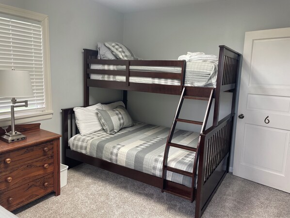 A bunk bed with a ladder, a bedside table with a lamp, a dresser, and a door with the number 6.