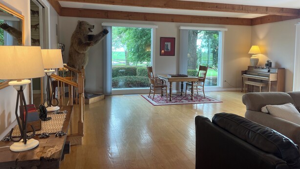 Una sala de estar con techo de madera, una zona de comedor con un piano y un ventanal con vistas al verdor.