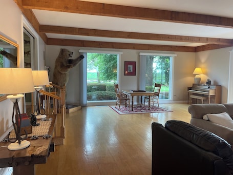 A living room with a wooden ceiling, a dining area with a piano, and a large window with a view of greenery.. Shallowbrook Farm: Where World-Record History Meets Private Luxury