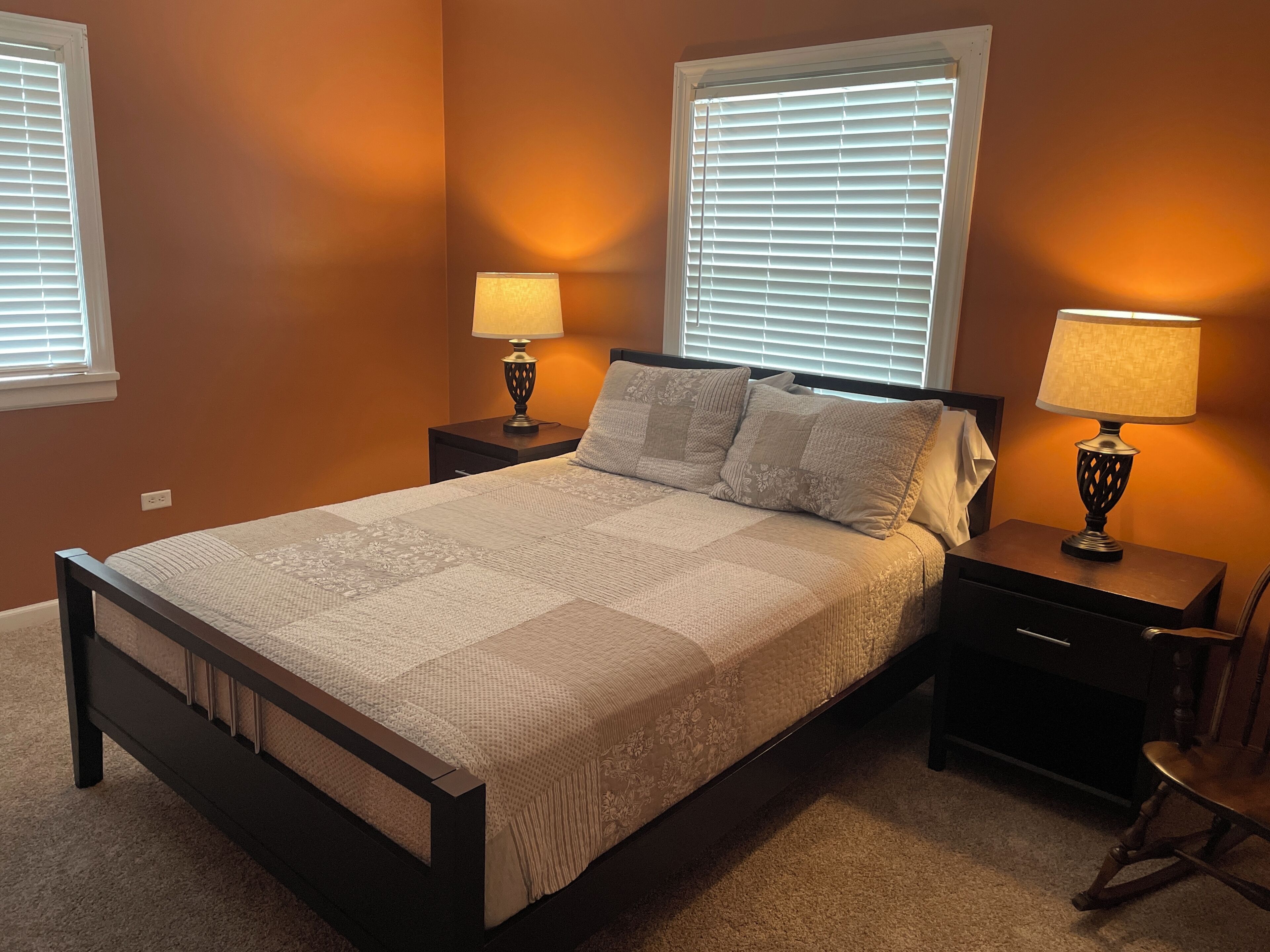 A bedroom with a bed, nightstands, lamps, and a chair.