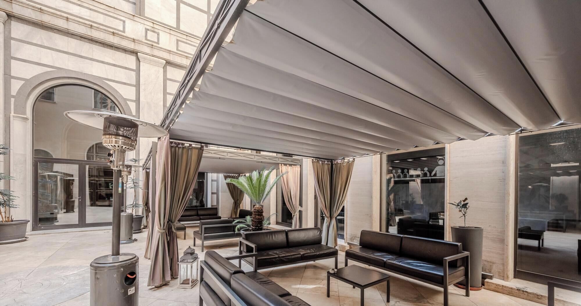 An outdoor seating area with a covered patio, leather sofas, and a trash can.