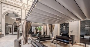 An outdoor seating area with a covered patio, leather sofas, and a trash can. - HOTIDAY Room Collection - Roma Cornelia (Rome)
