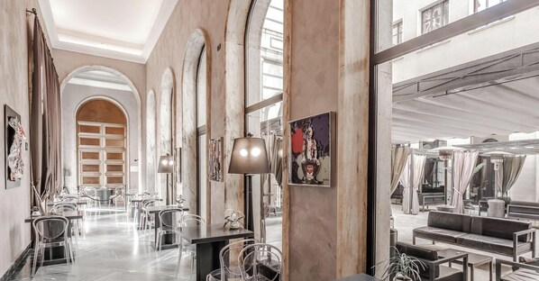A hotel lobby with marble columns, clear glass chairs, and a large mirror reflecting the interior. - HOTIDAY Room Collection - Roma Cornelia (Rome)