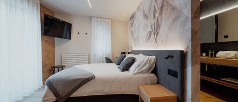 A modern bedroom with a large bed, bedside tables, a TV, and a bathroom with a mirror and sink.