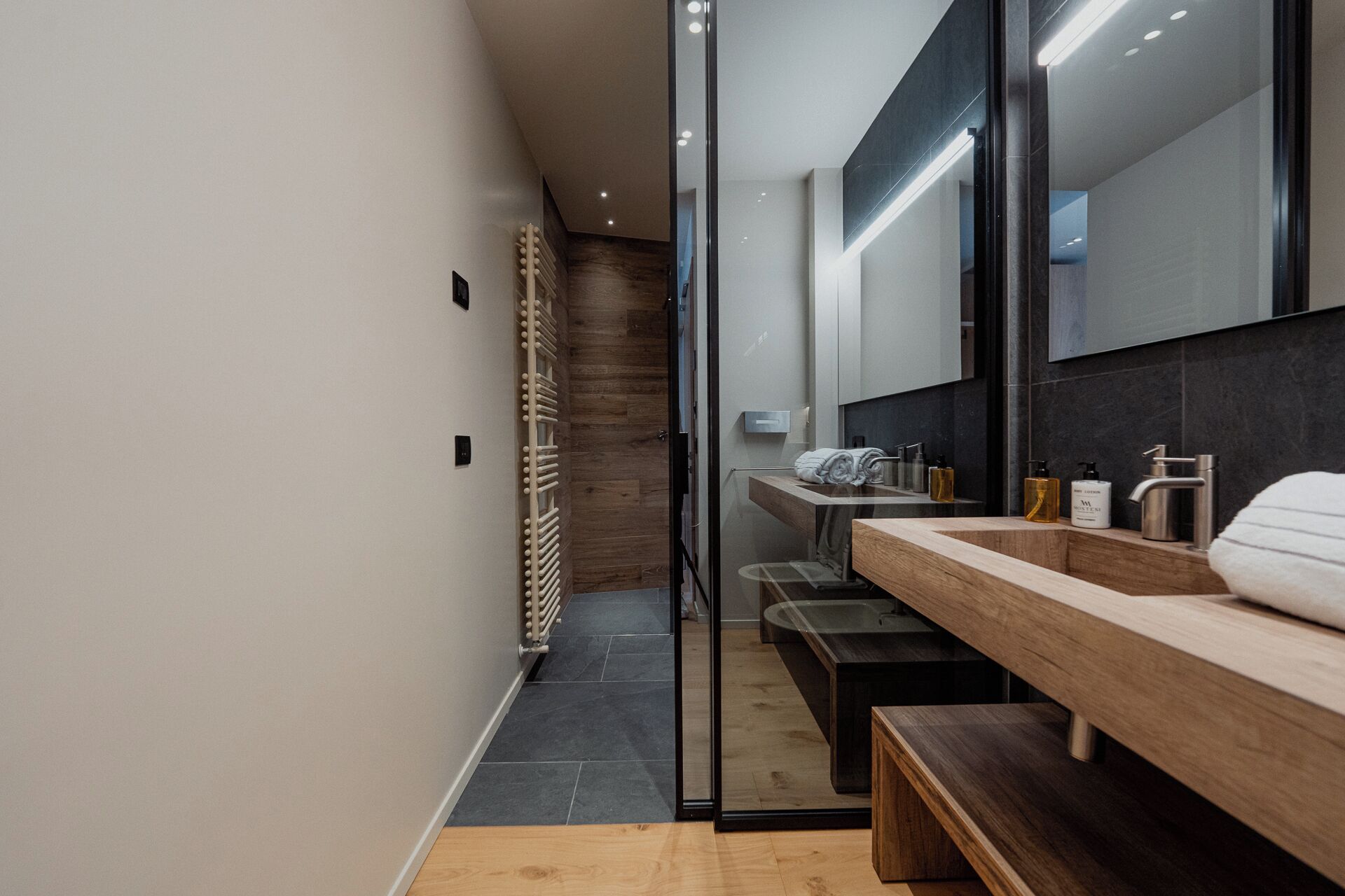 Une salle de bain moderne avec un banc en bois, une cabine de douche en verre et un grand miroir.