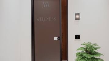 A door with "WELLNESS" engraved on it, a small potted plant, and a wall-mounted light fixture.