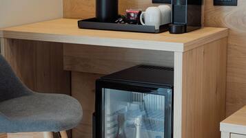 Une petite cuisine équipée comprenant un réfrigérateur contenant des boissons, une machine à café et une bouilloire, le tout posé sur un plan de travail en bois.