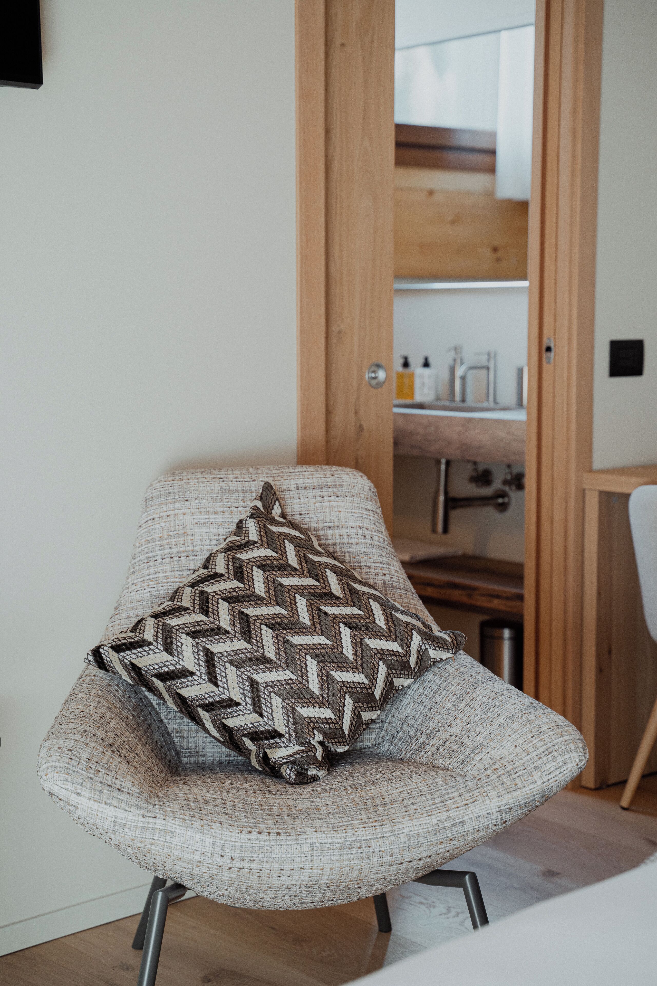 A chair with a patterned cushion in a room with a wooden door, a sink, and a mirror.