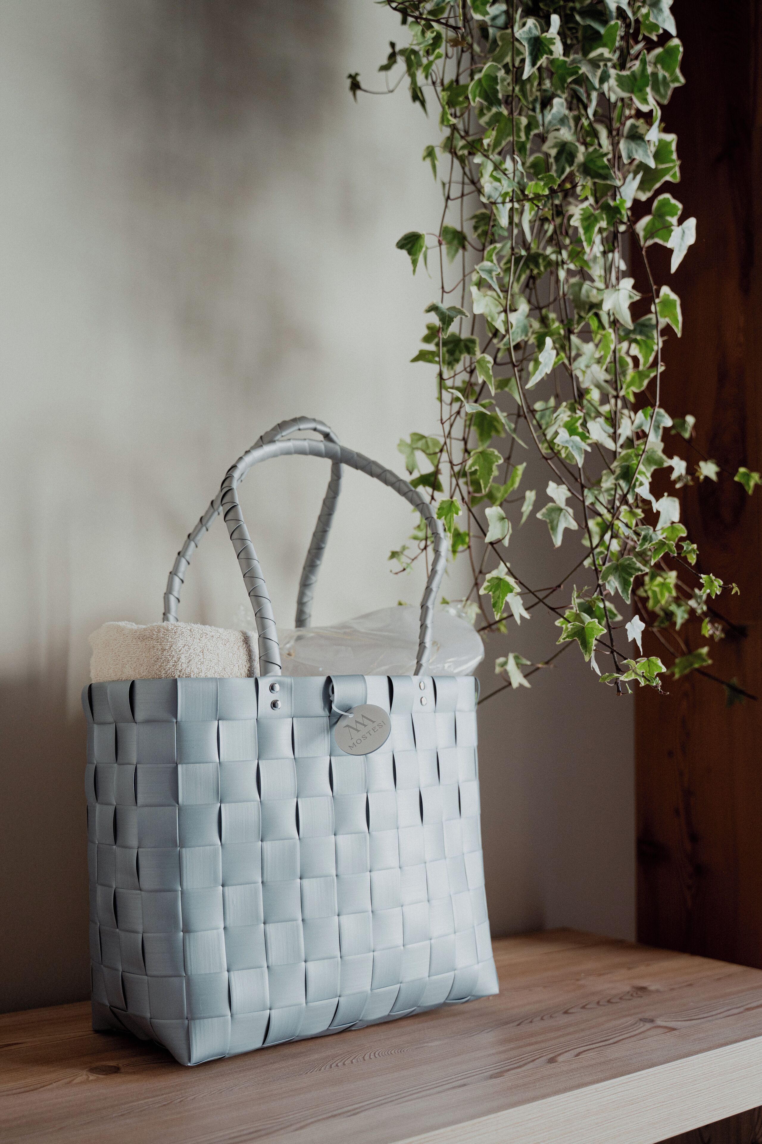 A grey woven bag with a handle and a white tag on a wooden shelf.