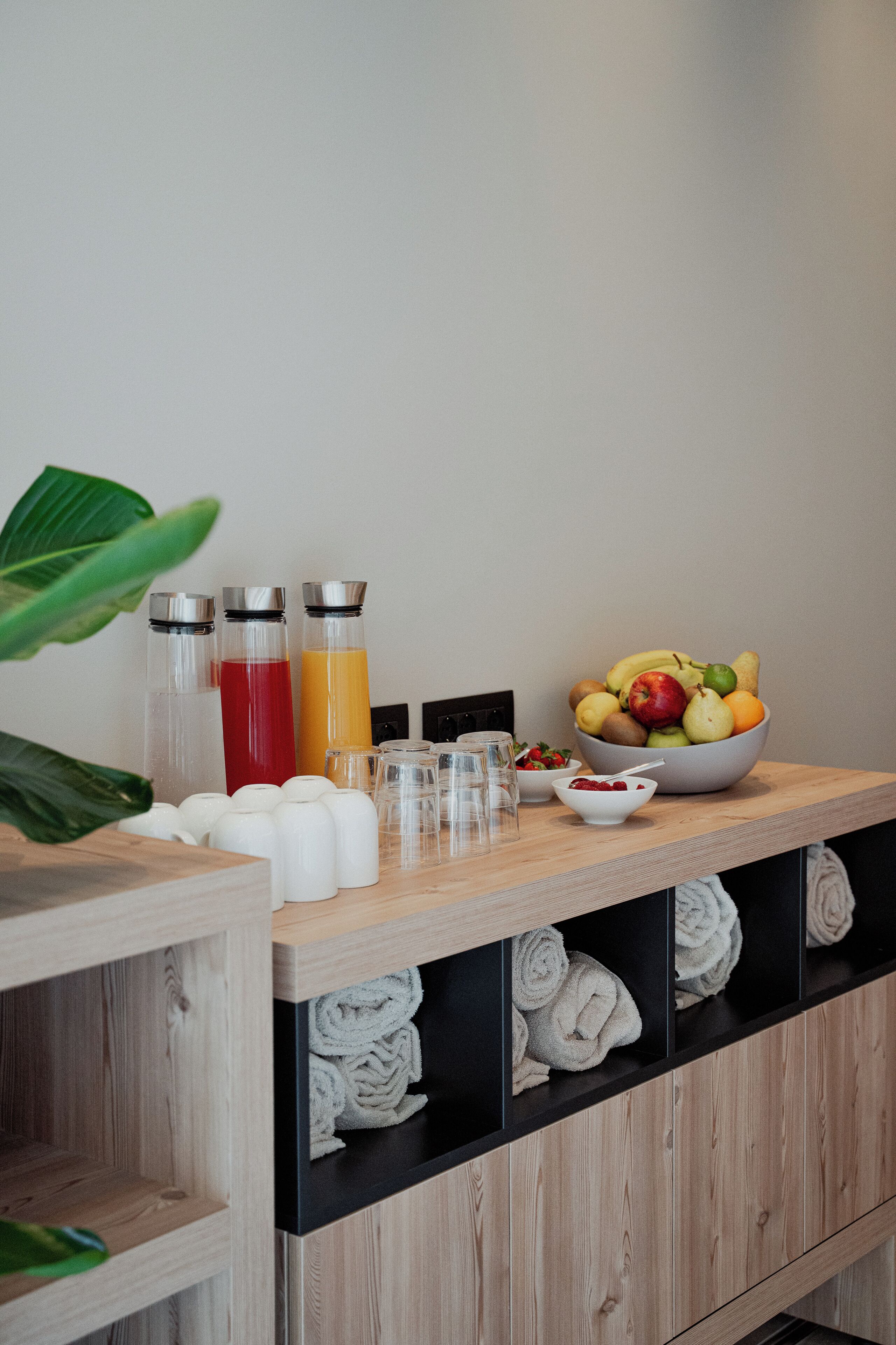 A wooden table with a fruit bowl, juice bottles, glasses, and towels.