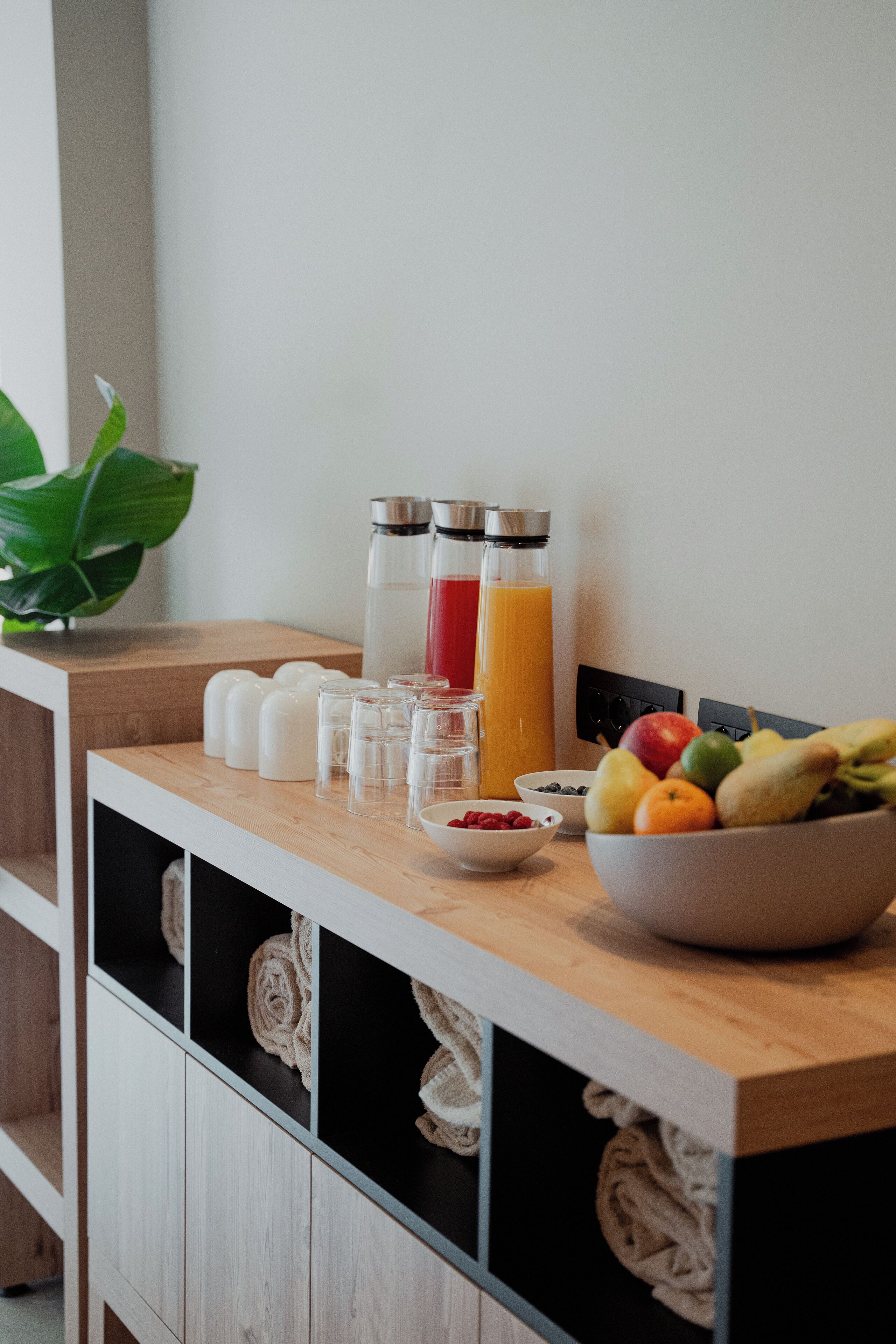 A breakfast setup with a wooden counter, a bowl of fruit, a glass of orange juice, and two bottles of water.