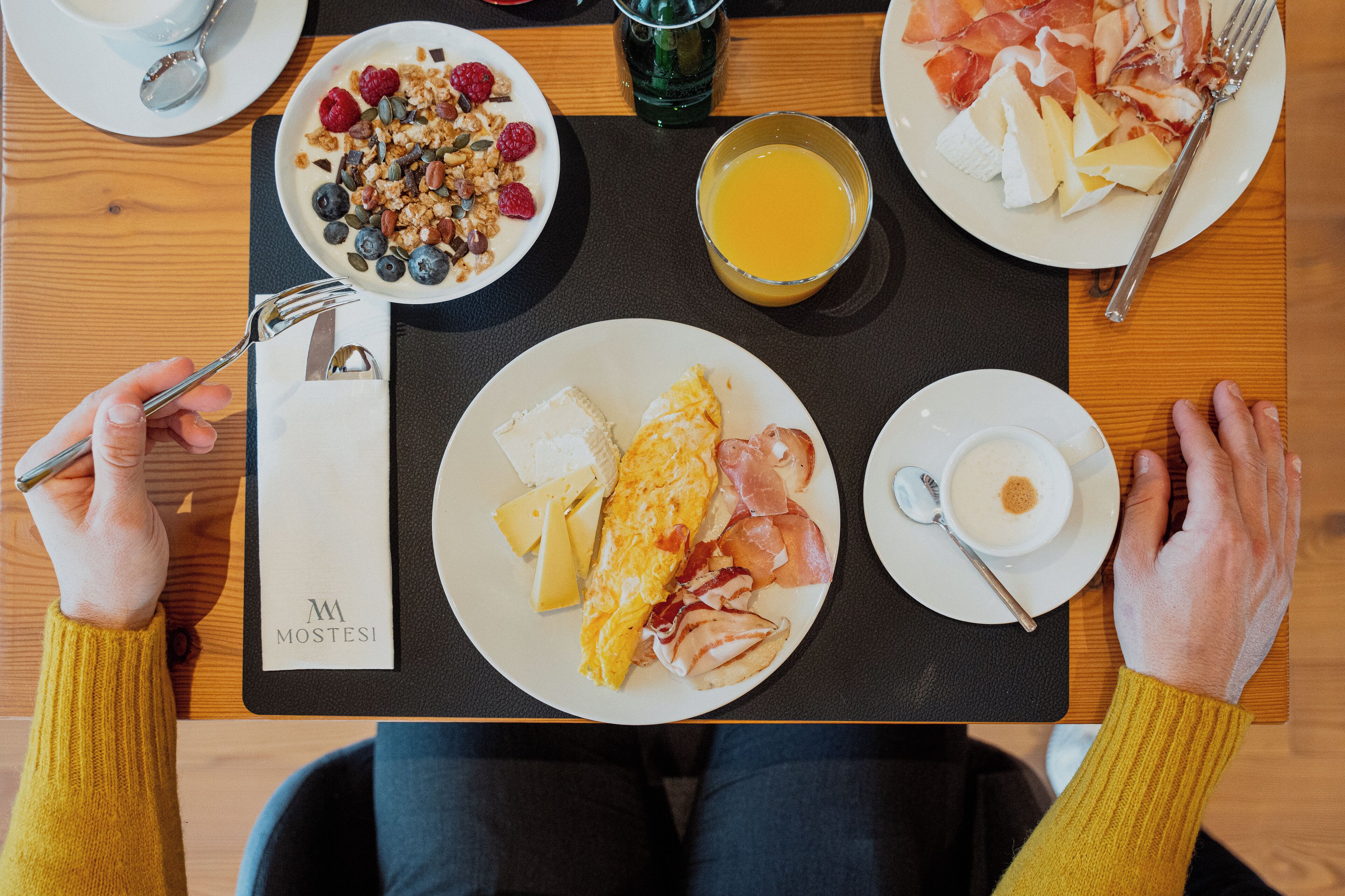 Un plateau de petit-déjeuner avec des œufs, du jambon, du fromage et des fruits, posé sur une table en bois.
