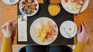 A breakfast tray with eggs, ham, cheese, and fruit on a wooden table.