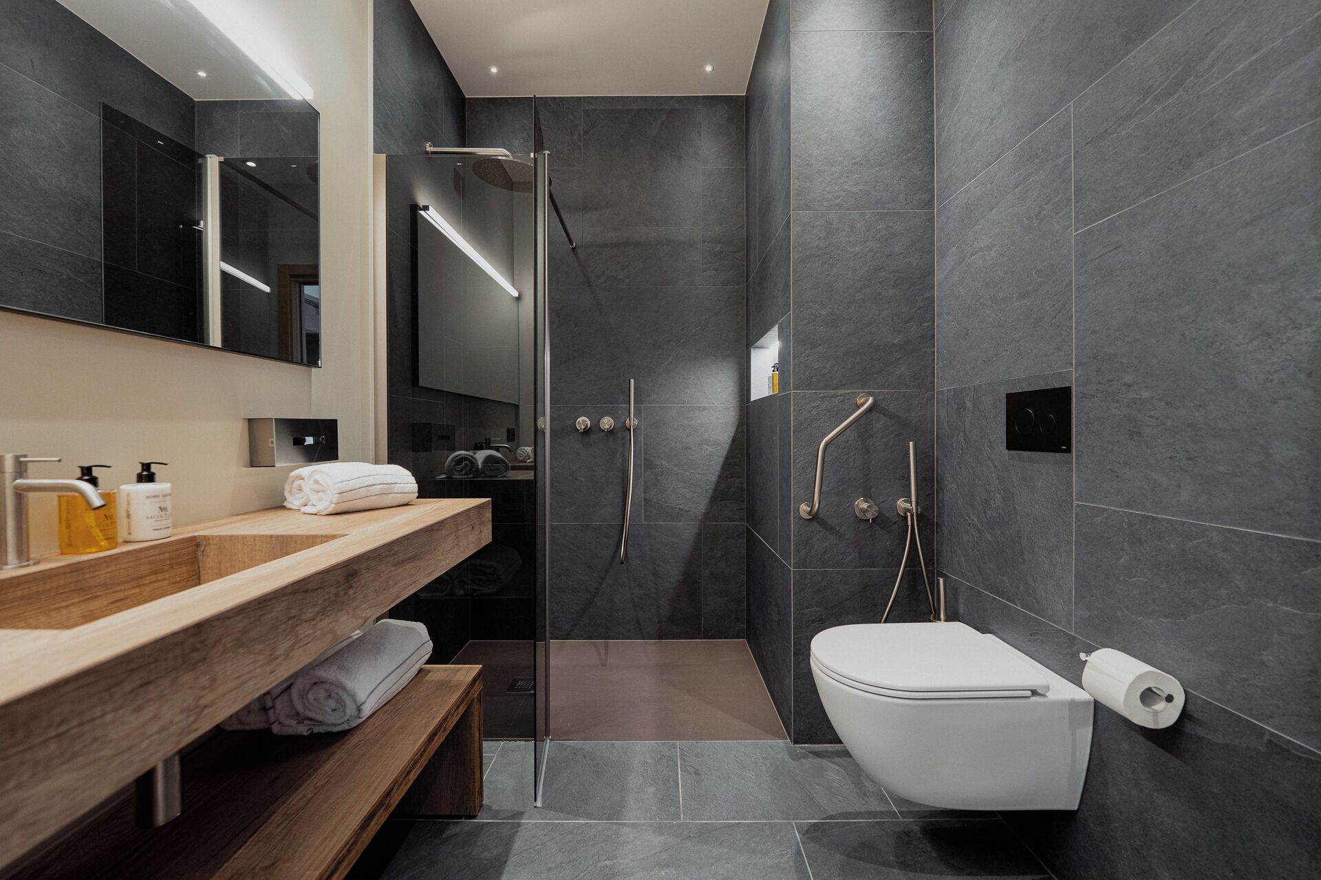 Un baño moderno con tocador de madera, mampara de ducha de vidrio y un inodoro blanco.