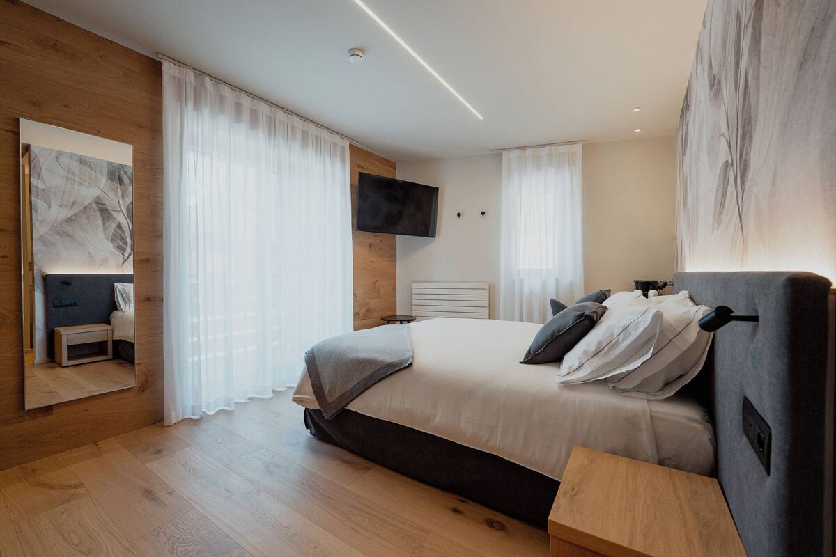 Et moderne soveværelse med en stor seng, et ophængt fjernsyn og trægulv.