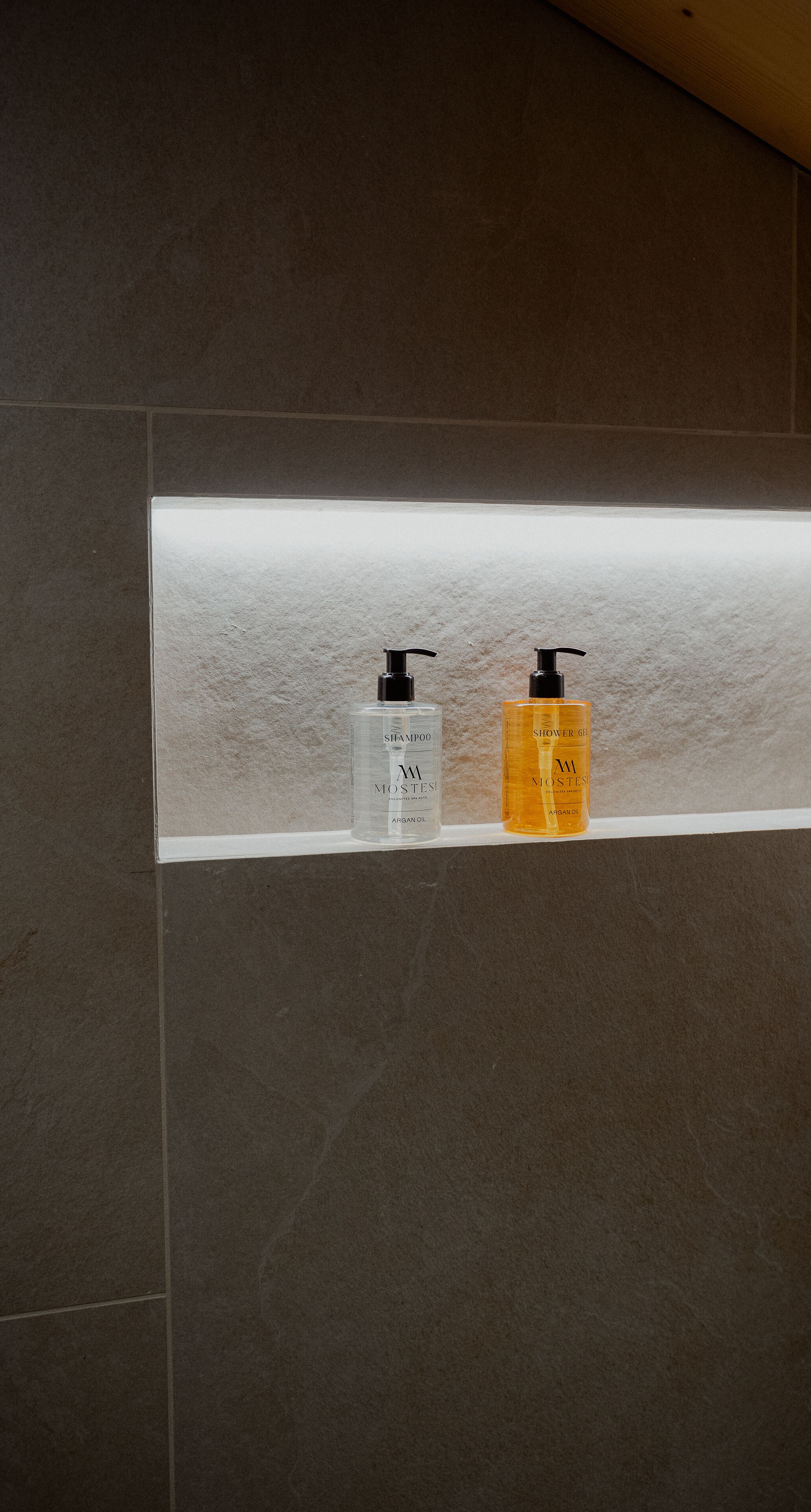 Ein Badezimmer mit gefliesten Wänden und einem Regal mit zwei Shampoo- und Duschgelflaschen.