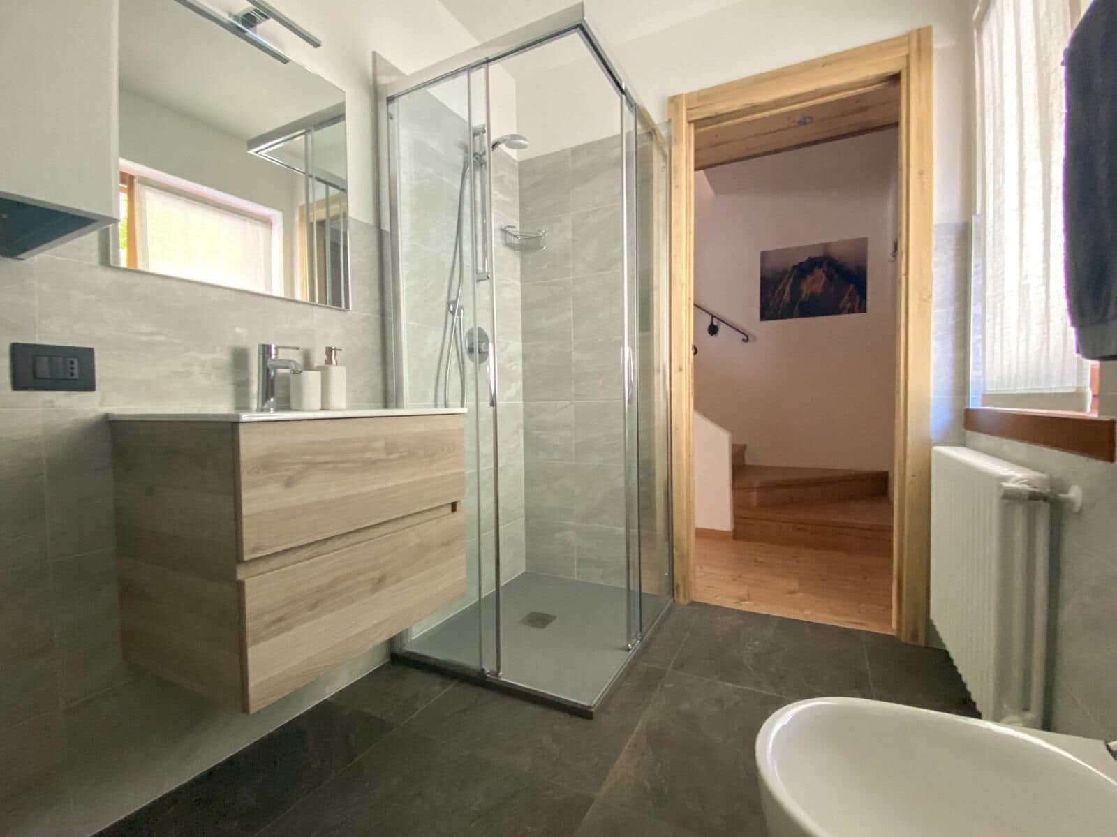 A modern bathroom with a glass shower enclosure, a wooden vanity, and a white bathtub.