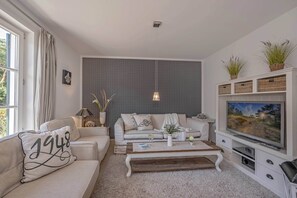 Un soggiorno con divano, tavolino, televisione e piante ornamentali.