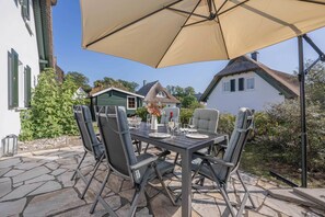 Un'area pranzo all'aperto con un tavolo imbandito per quattro persone, circondato da sedie, sotto un grande ombrellone.