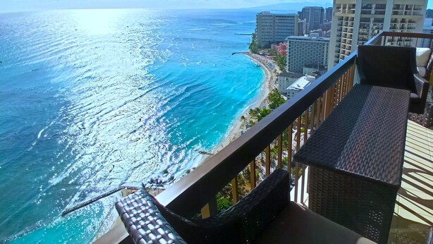 Ein Balkon mit Blick auf Strand und Meer, ein Stuhl und ein Geländer.
