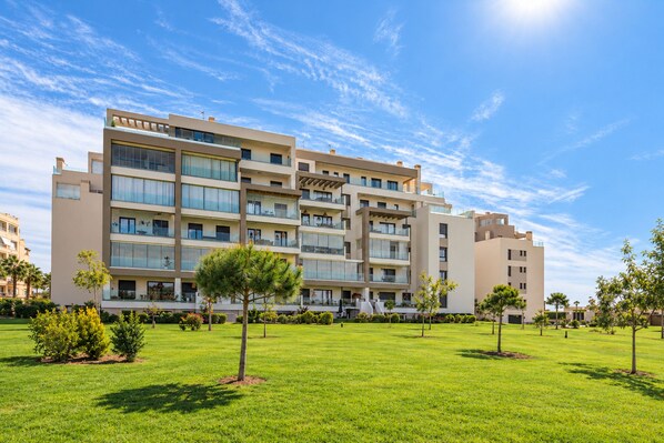 A multi-story hotel with a flat roof, large windows, and a well-maintained lawn with young trees.