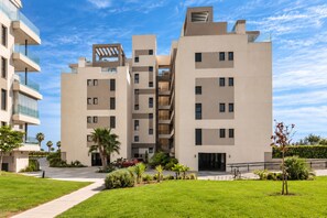 Un edificio residencial moderno de varios pisos con balcones, un patio central y zonas verdes circundantes.