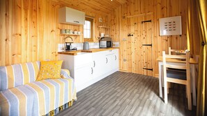 A cozy wooden cabin interior with a sofa, kitchen area, and dining table. - Head For The Hills Glamping Shepherd’s Hut. Pet friendly, mountain views

 (Llanfynydd)