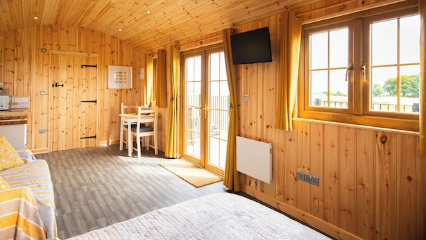 A wooden cabin interior with a bed, a desk, a chair, and a television mounted on the wall. - Head For The Hills Glamping Shepherd’s Hut. Pet friendly, mountain views

 (Llanfynydd)