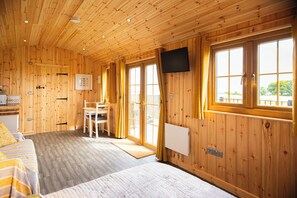 L’intérieur d’une cabane en bois, avec un lit, un bureau, une chaise et un téléviseur fixé au mur.