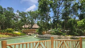 A pool area with a wooden fence, surrounded by lush greenery and a small building in the background. - 2 Bedroom Estates 5 Diamonds, VIP Golf Tournament, VIP Park Access Vidanta World (Nuevo Vallarta)