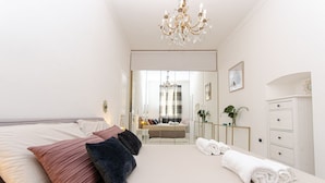 A modern bedroom with a large bed, a chandelier, a mirror, and a view into another room. - VivimiHome - Rifugio Chic a Milano Buenos Aires (Milano)