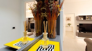A modern living room with a yellow and black geometric coffee table, a large vase with dried plants, and a television in the background. - VivimiHome - Rifugio Chic a Milano Buenos Aires (Milano)