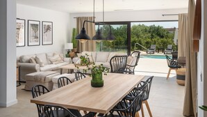 A modern living room with a wooden dining table, black chairs, a sofa, and a view of a swimming pool.